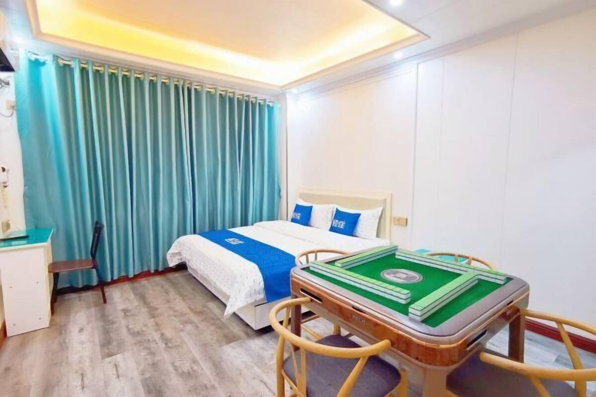 A hotel room with a bed, a desk, a chair, and a table with a green board game.