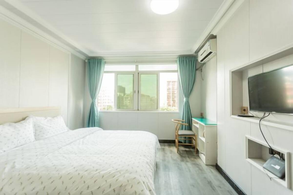 A hotel room with a bed, a desk, a chair, a television, and a window with curtains.