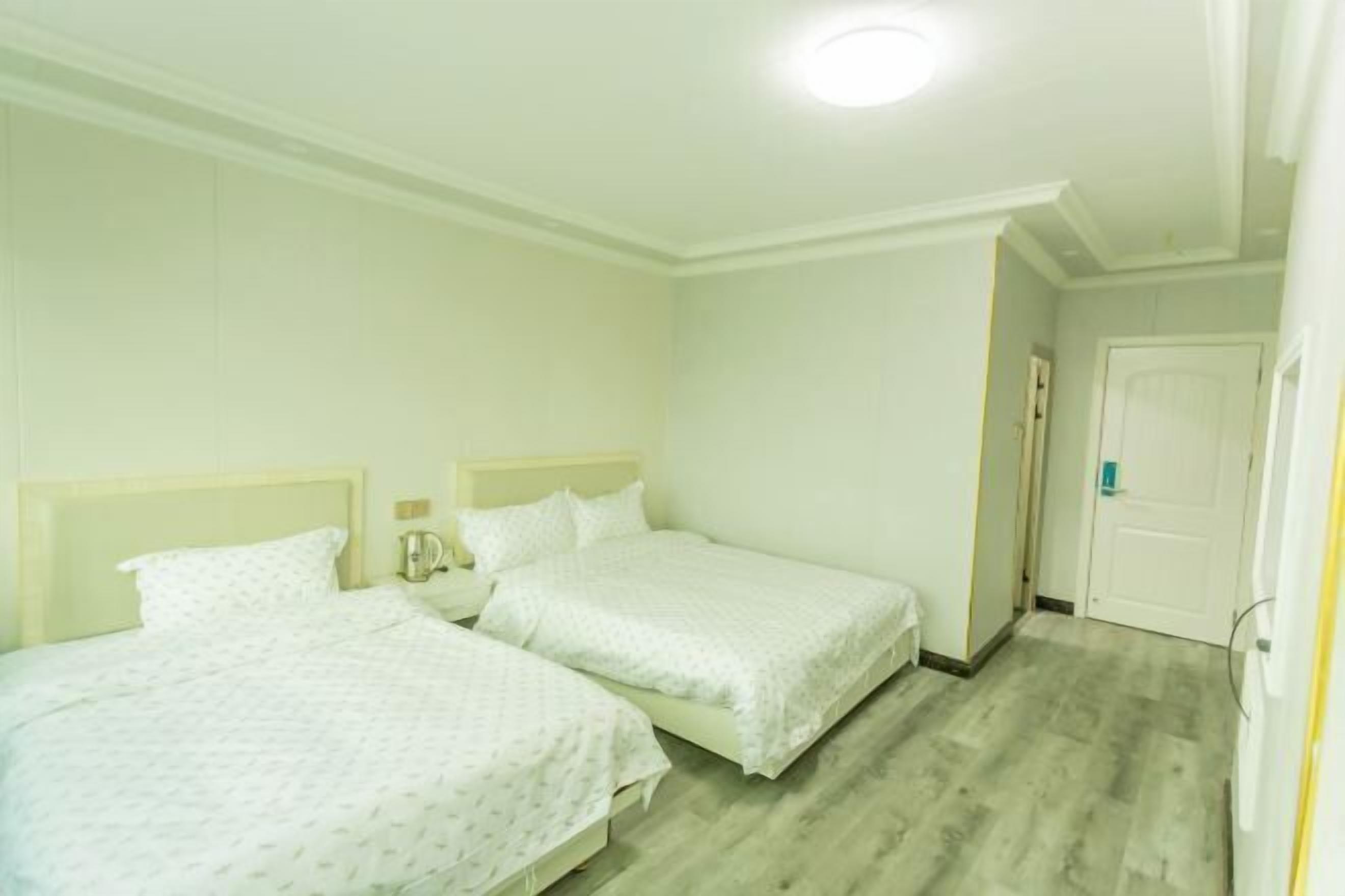 A hotel room with two beds, a small bedside table, a nightstand, and a door.