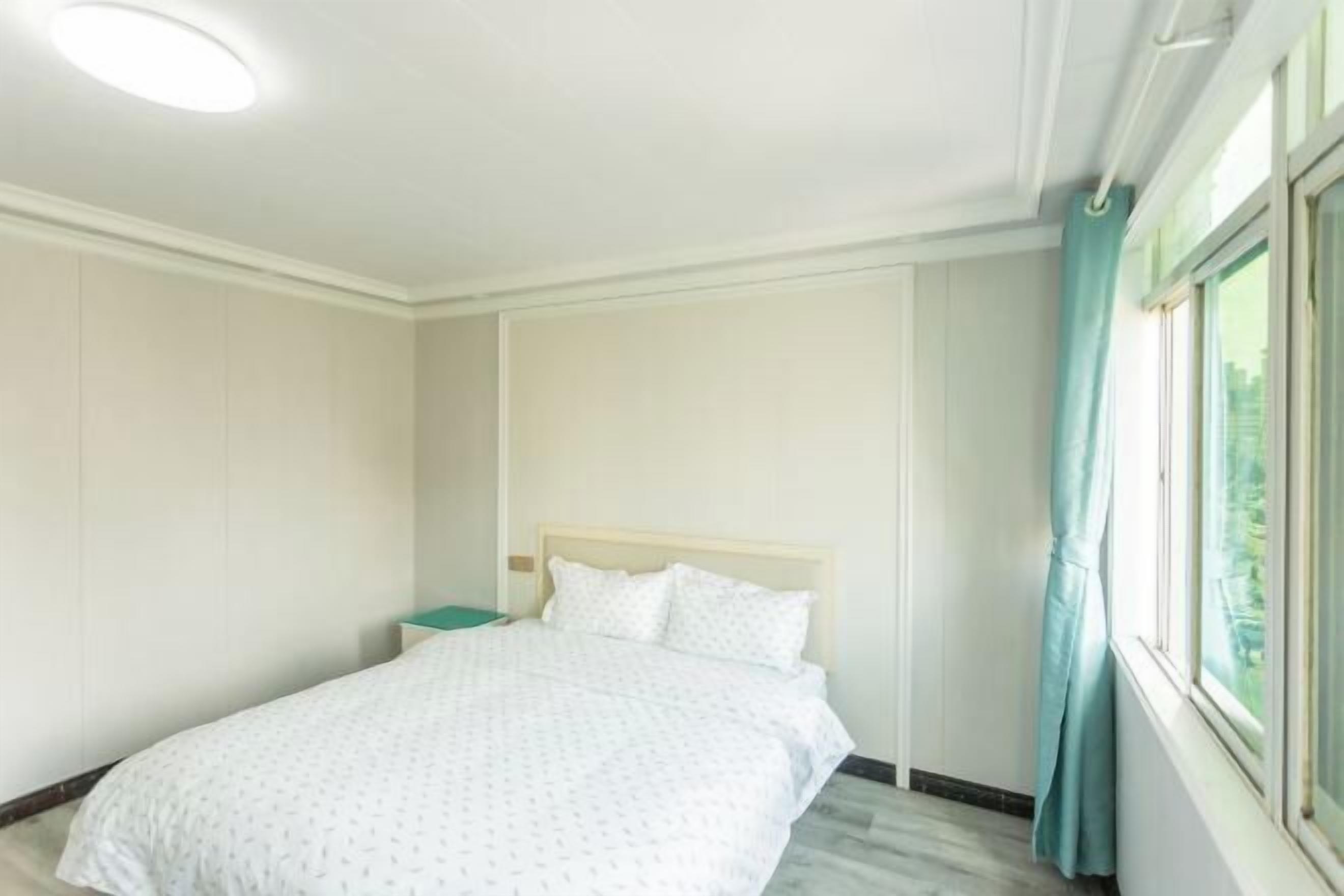 Una habitación de hotel con una cama, una mesita de noche, una ventana con cortinas y una lámpara en el techo.