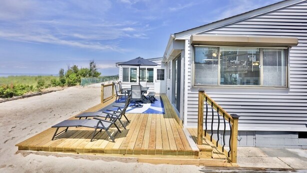 Una casa de playa con terraza, muebles de exterior y vista al mar.