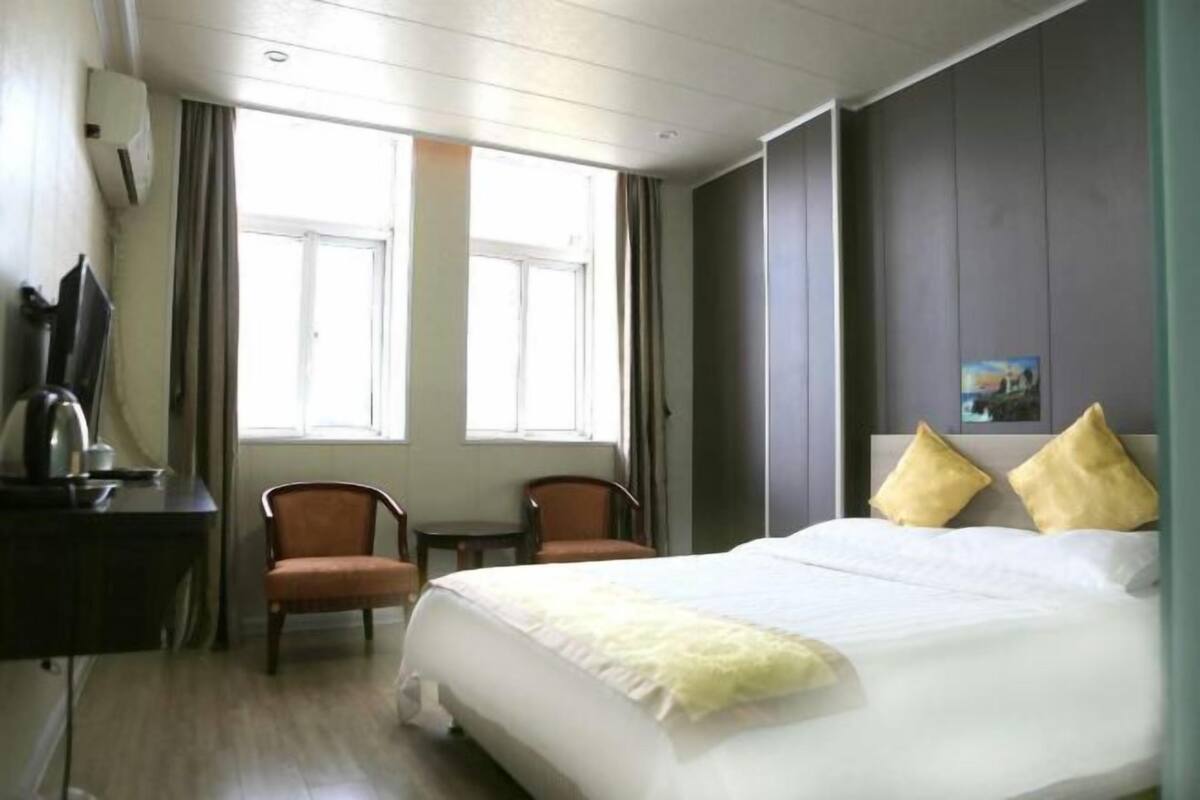 A hotel room with a bed, two chairs, a desk with a kettle, and a window.