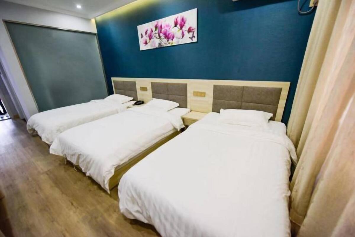 A hotel room with three single beds, a blue accent wall, and a floral painting.