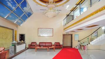 A hotel lobby with a red carpet, a reception desk, seating area, and a staircase.