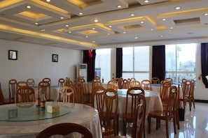 Un salón de conferencias con mesas y sillas redondas, ventanas amplias con cortinas e iluminación empotrada en el techo.