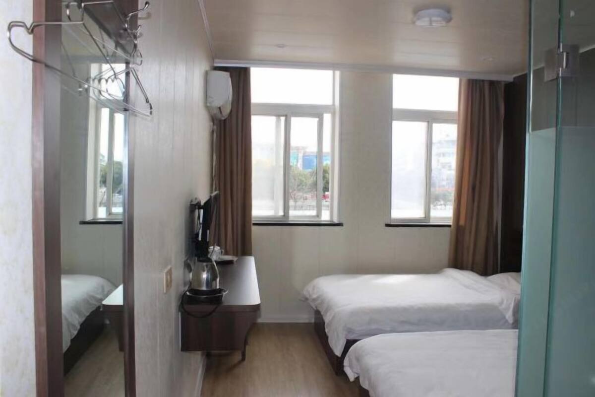 A hotel room with two beds, a desk with a lamp, a mirror, and windows with curtains.