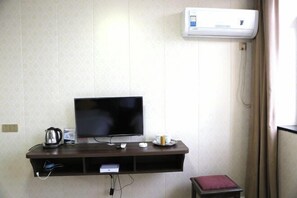 Una habitación con una televisión de pantalla plana en un estante fijado a la pared, una tetera, un control remoto y una pequeña mesa con una vela.