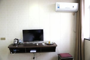 Una habitación con una televisión de pantalla plana en un estante fijado a la pared, una tetera, un control remoto y una pequeña mesa con una vela.