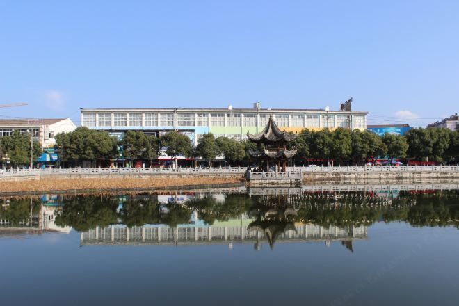 Um edifício tradicional refletido na água, com uma ponte e árvores ao primeiro plano.