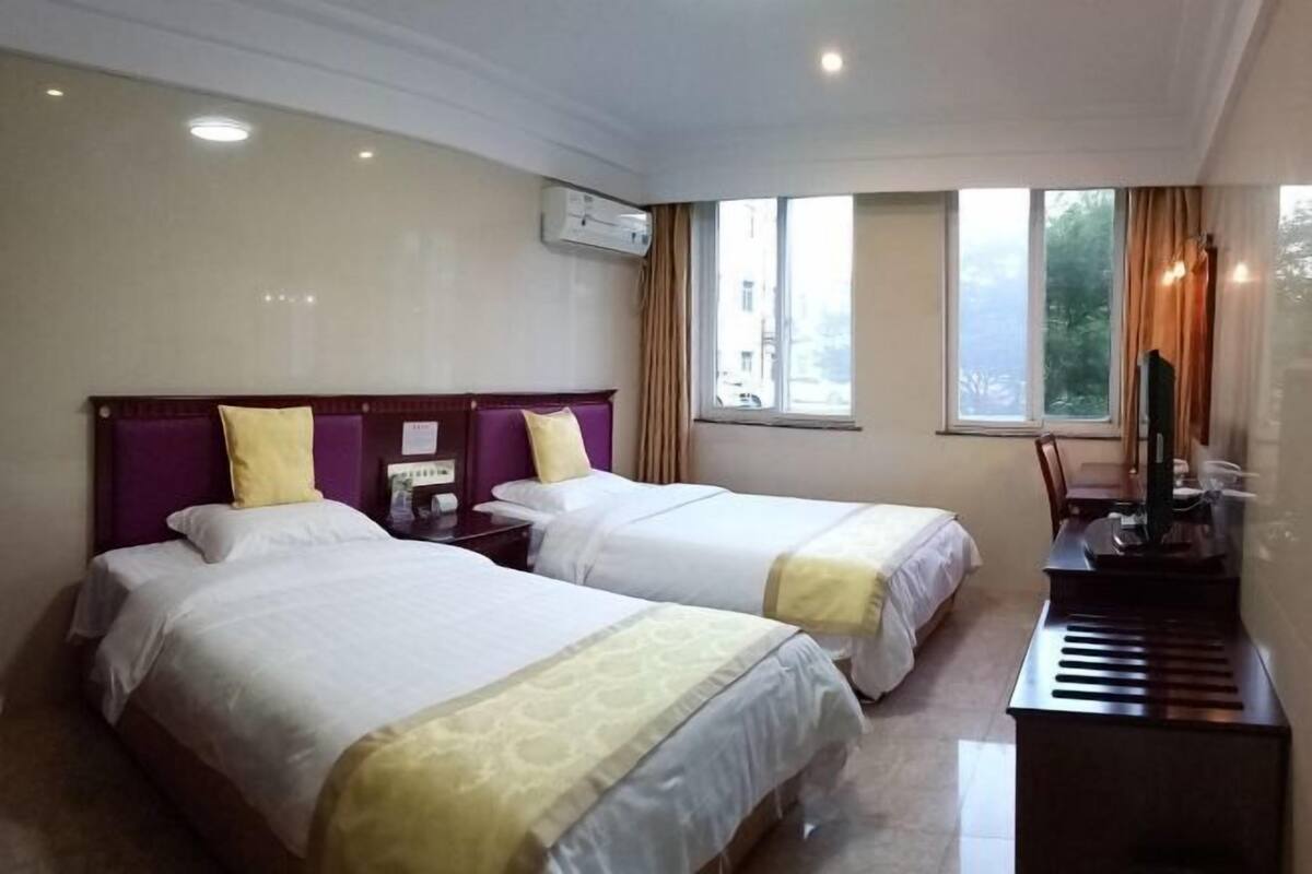 A hotel room with two beds, a desk, a chair, and a window with curtains.