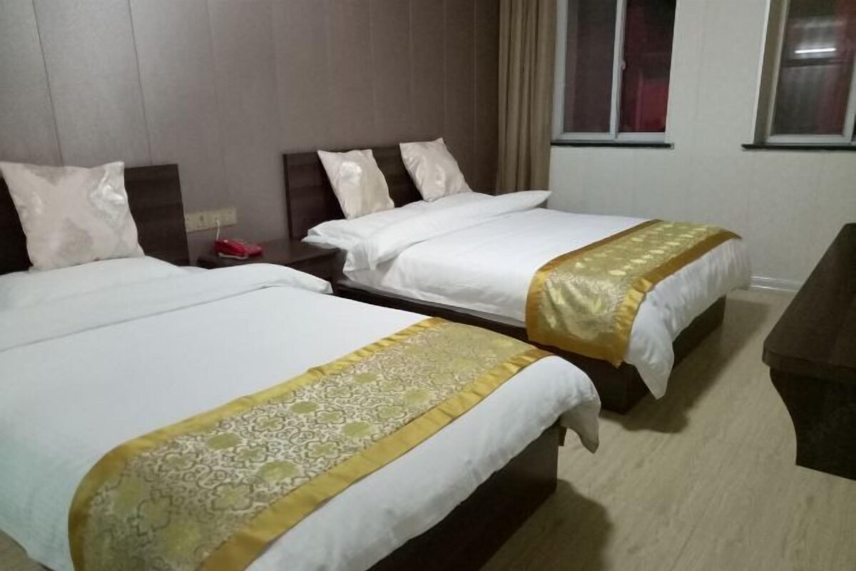 Habitación de hotel con dos camas, cada una con cubrecama blanco y detalles dorados decorativos.