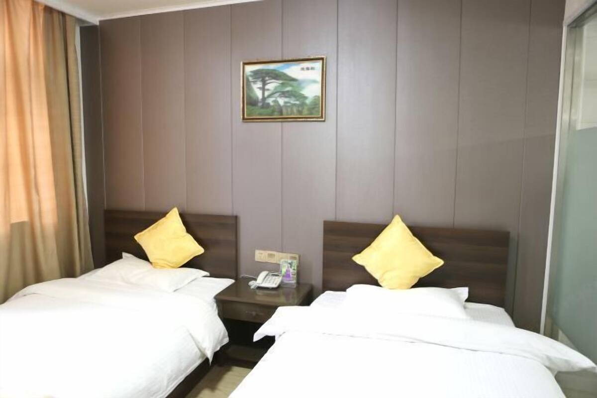 A hotel room with two beds, each with a pillow, a nightstand with a phone, and a framed picture on the wall.