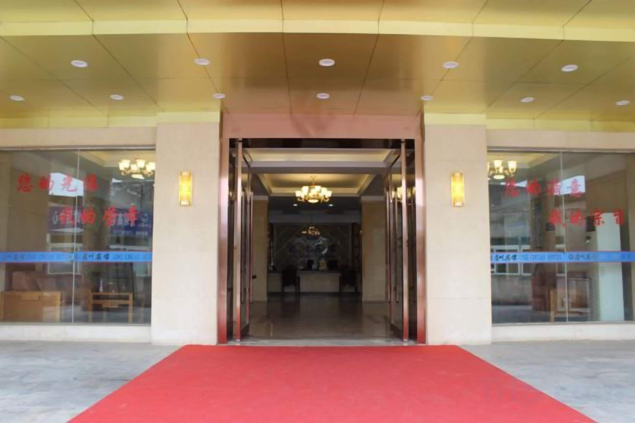 A hotel entrance with a red carpet, glass doors, and a chandelier.