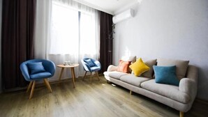 A modern living room with a sofa, two chairs, a small table, and a large window with curtains.