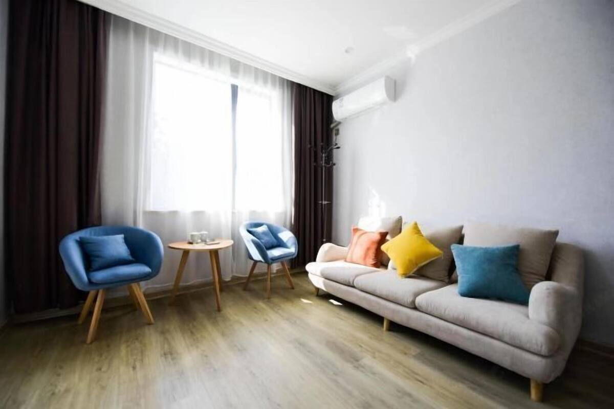 A modern living room with a sofa, two chairs, a small table, and a large window with curtains.