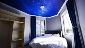A bedroom with a starry ceiling, a bed, a wardrobe, and a window with curtains.