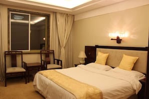 Habitación de hotel con cama, dos sillas, mesita de noche, lámpara y ventana con cortinas.