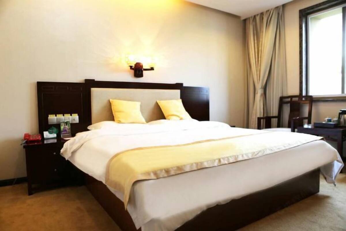 A hotel room with a large bed, a bedside table with a lamp, and a window with curtains.