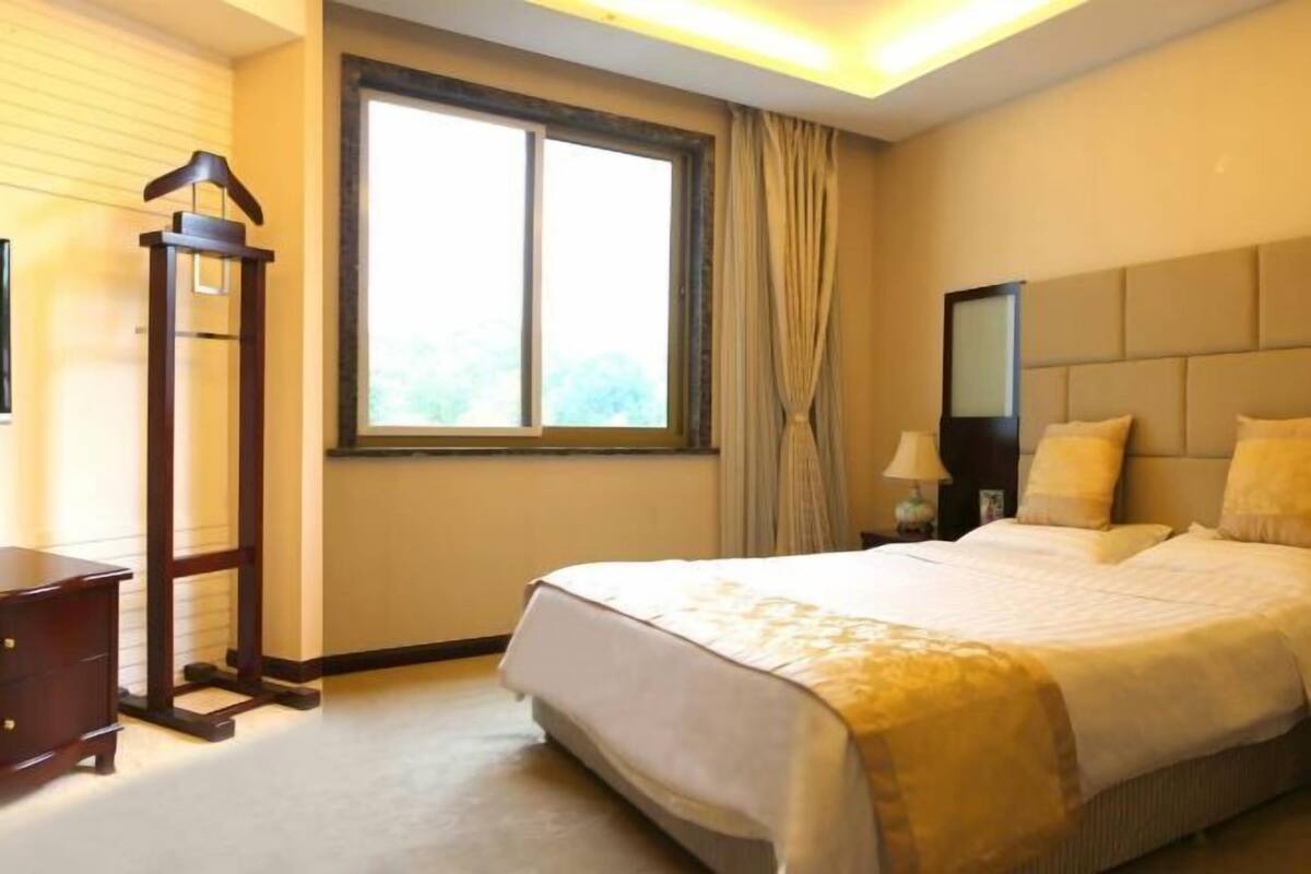 A hotel room with a bed, a nightstand, a lamp, a window with curtains, and a wooden floor.