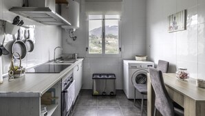 A compact kitchen with a window, a washing machine, and a dining area. - Cosy and Bright in La Arena Beach (Zierbena)