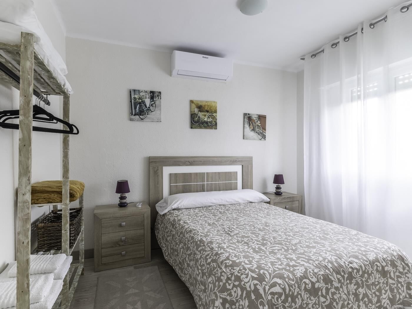 Een slaapkamer met een stapelbed, een enkel bed, een nachtkastje met een lamp, en een luchtverkoeler aan de muur.