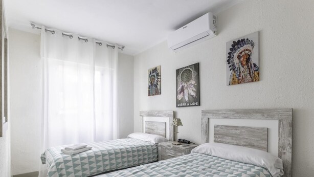 A hotel room with two beds, a window with sheer curtains, an air conditioning unit, and three wall art pieces. - Cosy and Bright in La Arena Beach (Zierbena)