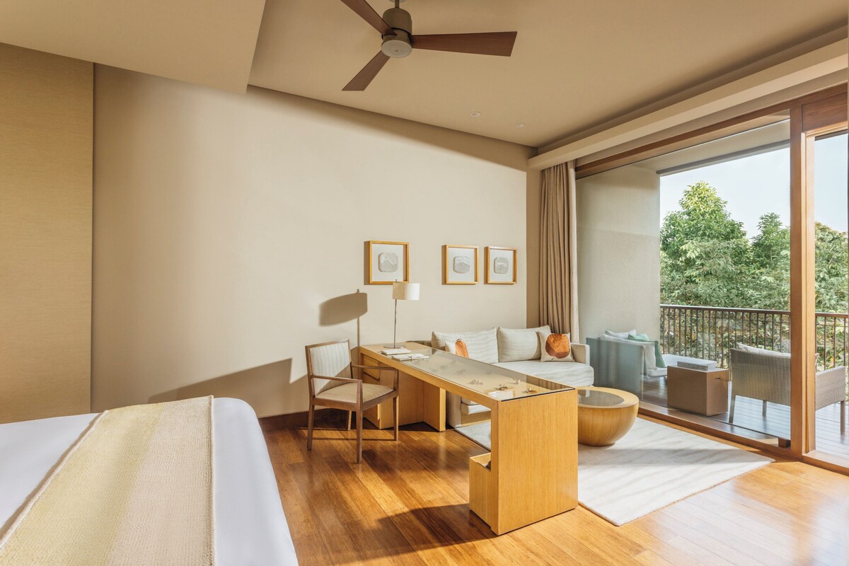 Habitación de hotel con cama, escritorio, silla, balcón amoblado y ventilador de techo.