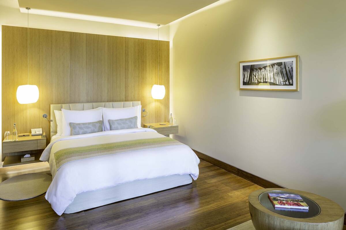 Una habitación de hotel moderna con una cama grande, mesitas de noche y una mesita redonda de madera con un libro.