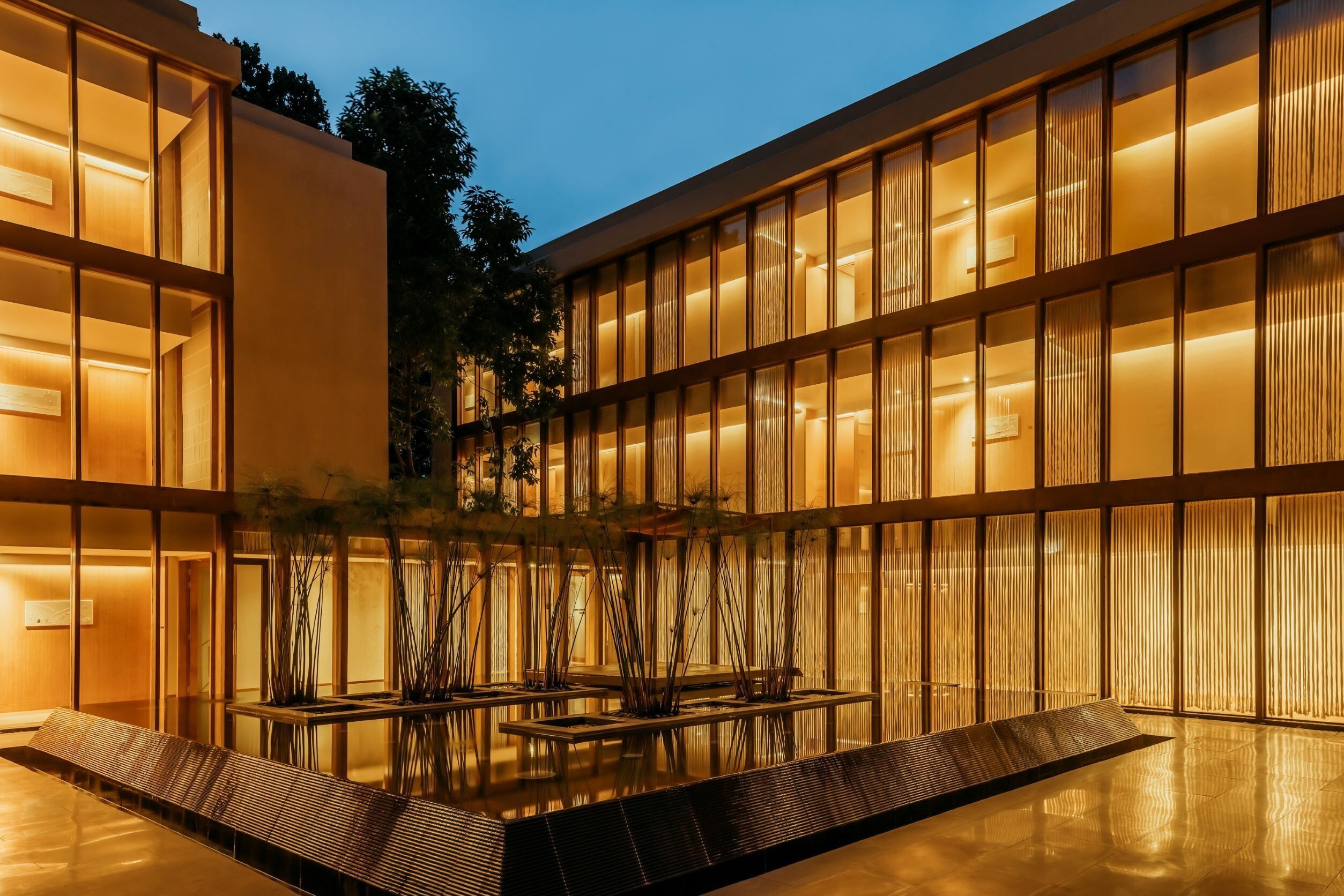 A modern building with a courtyard, featuring a reflective pool and seating areas.