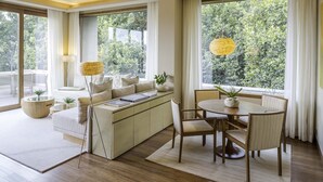 A modern living room with a sofa, dining table, and chairs, large windows with curtains, and a hanging lamp. - Six Senses Vana - A Wellness Retreat (Dehradun)