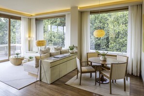 Un salon moderne comprenant un canapé, une table à manger et des chaises, de grandes fenêtres avec des rideaux et une lampe suspendue.