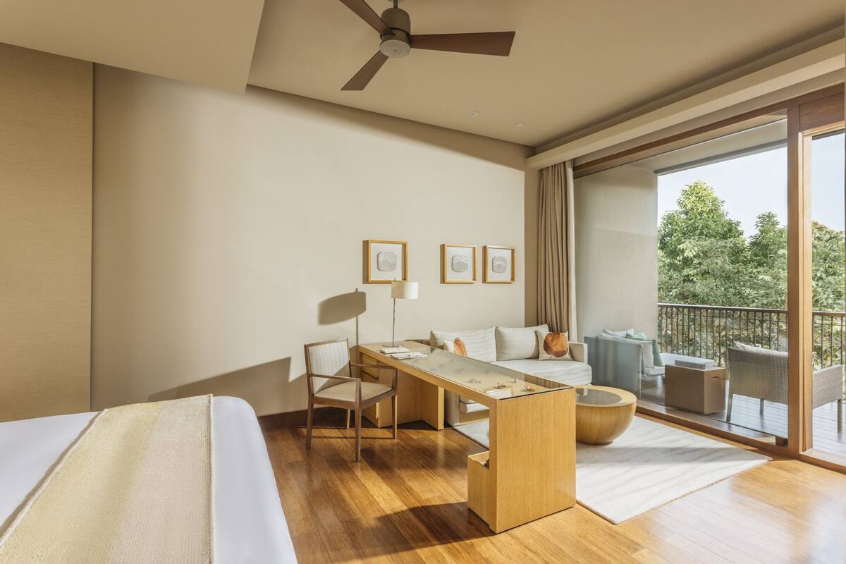 Una habitación de hotel moderna con cama, escritorio y balcón con mobiliario exterior.