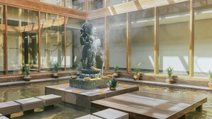 A tranquil indoor water feature with a statue, surrounded by wooden benches and potted plants. - Six Senses Vana - A Wellness Retreat (Dehradun)