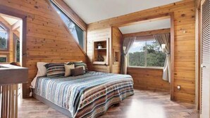Une chambre avec un plafond en pente en bois, un lit avec une literie à motifs, une table de chevet et une fenêtre avec des rideaux.