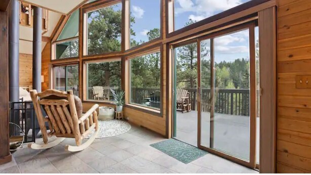Une pièce spacieuse avec de grandes fenêtres, un fauteuil à bascule en bois et une vue sur l’extérieur.