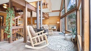 Un intérieur chaleureux avec un fauteuil à bascule en bois, un tapis rond et une grande fenêtre donnant sur l’extérieur.