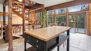 Une pièce spacieuse avec une grande table en bois, un escalier en colimaçon et de grandes fenêtres donnant sur l’extérieur.