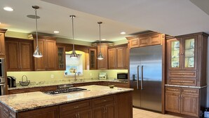 A modern kitchen with wooden cabinets, a large island, stainless steel appliances, and pendant lighting. - Stunning Water Front Home with Private Dock and Beach and Sunsets (Lusby)