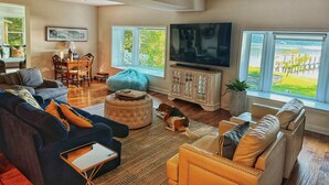 A spacious living room with a large TV, comfortable seating, and a view of a water body. - Stunning Water Front Home with Private Dock and Beach and Sunsets (Lusby)