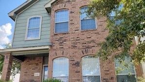 A two-story brick building with a green front porch, a small front yard with a bush, and a visible address sign.