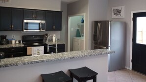A modern kitchen with dark cabinets, a microwave, stove, refrigerator, and granite countertop.