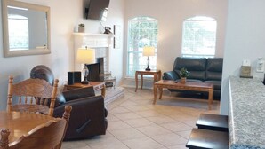 A living room with a fireplace, a sofa, a dining table, and a TV mounted on the wall.