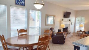 A spacious living room with a fireplace, a dining area with wooden chairs, and a kitchen with a large island.