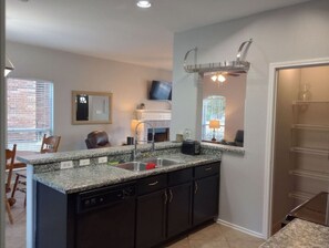 A kitchen with granite countertops, dark cabinetry, a dishwasher, a sink, a built-in oven, and a window with blinds.