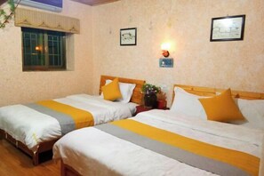 A hotel room with two beds, each with a wooden headboard, white and gray bedding, and yellow accents. There is a small table with a vase of flowers, a wall-mounted light, and two framed pictures on the wall. - Yuerong Inn (Nanjing County)