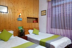 A hotel room with two beds, wooden paneling, a small shelf with items, a wall-mounted light, and a window with curtains. - Yuerong Inn (Nanjing County)