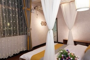 A hotel room with a bed, curtains, a bedside table, a lamp, and a floral arrangement. - Yuerong Inn (Nanjing County)
