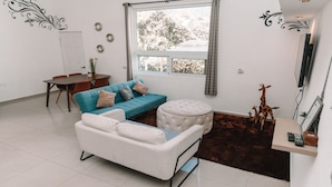 Una sala de estar moderna con sofá, reposapiés y un comedor con mesa y sillas.
