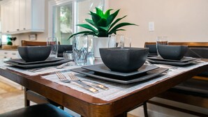 A dining table set with black bowls, plates, and cutlery, a vase with a plant, and a window in the background.