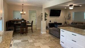 A spacious kitchen with a dining area, a living room with a sofa, and a TV mounted on the wall.